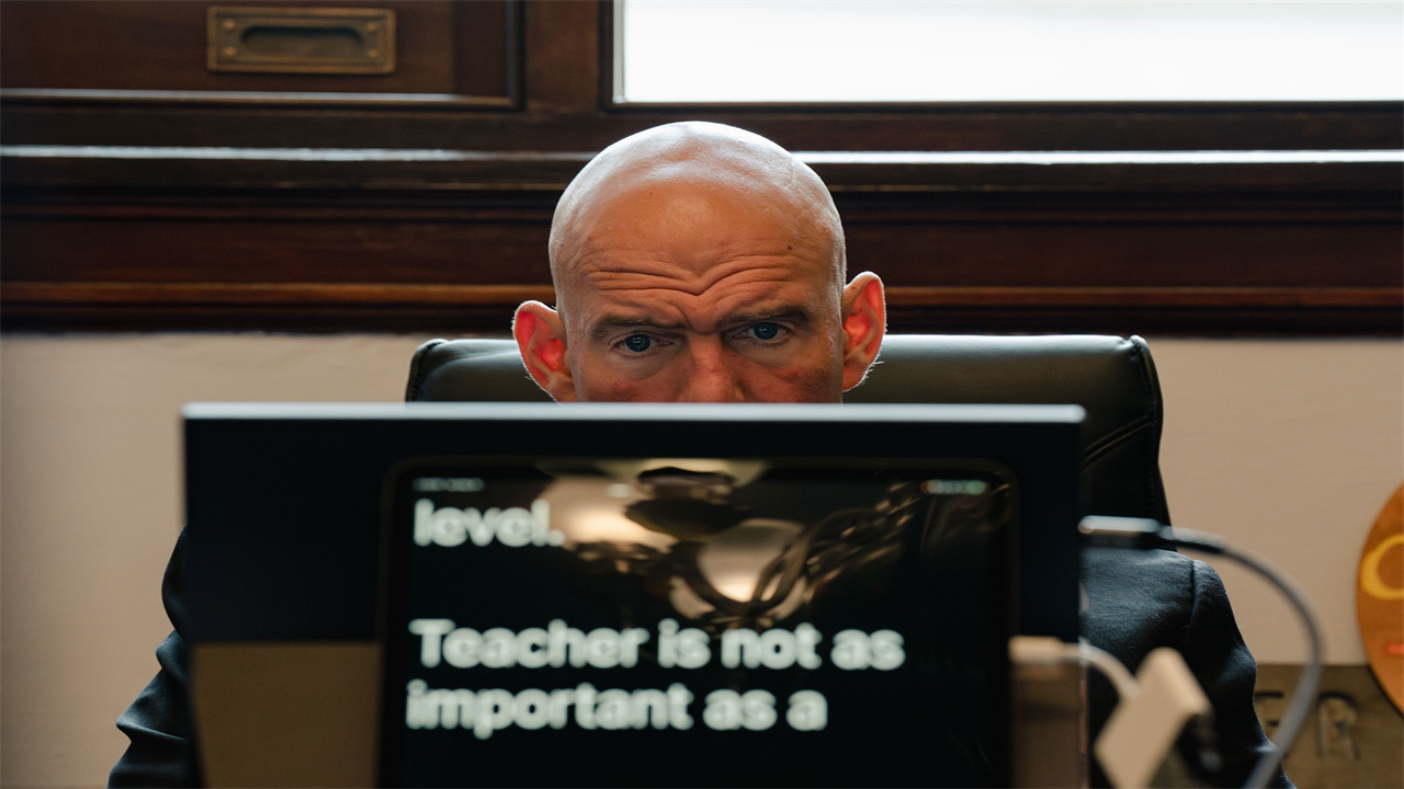 Senator John Fetterman reads from a closed captions prompter with a concentrated look on his face as he sits as his desk
